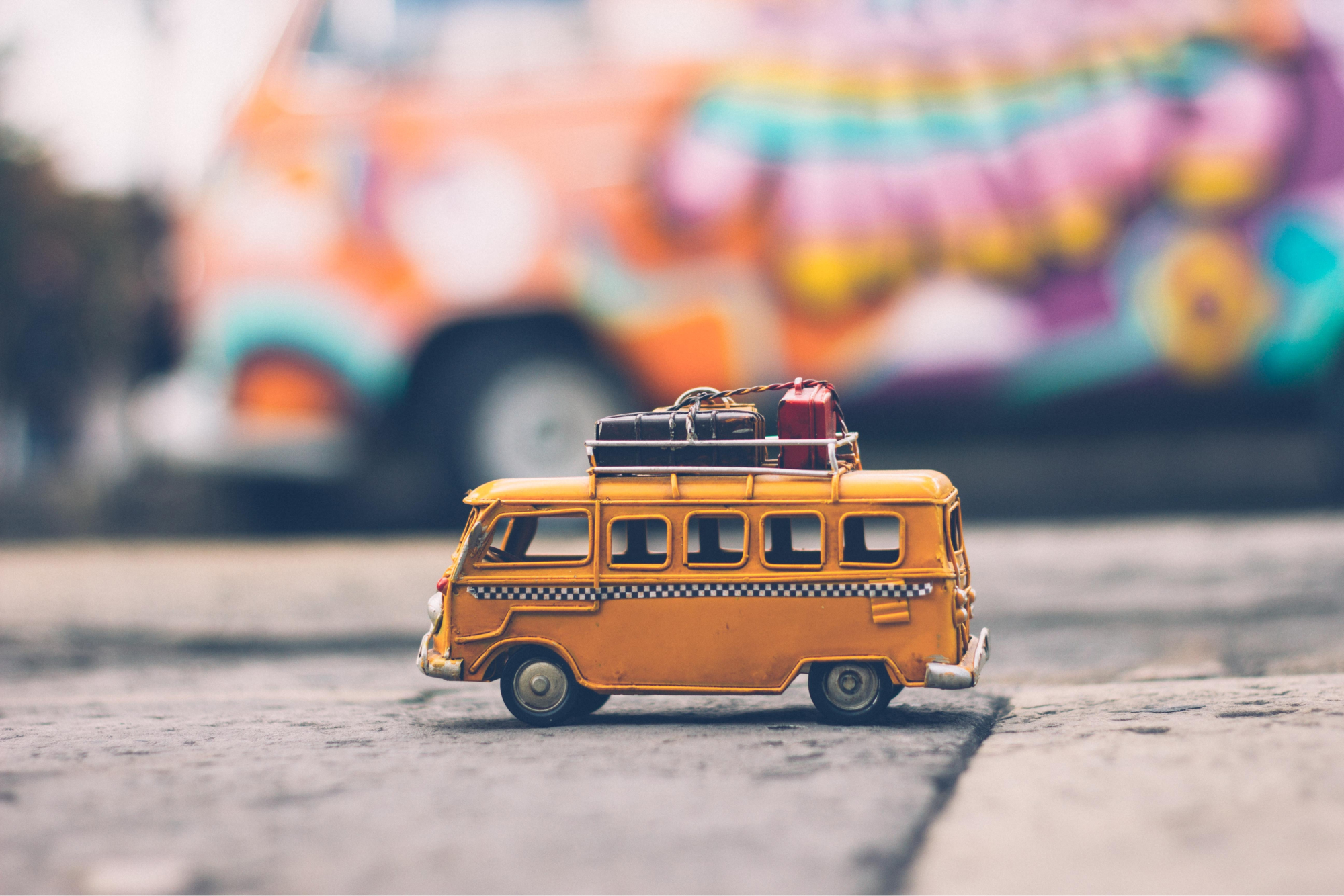 Miniature yellow bus zoomed in with large colorful blurred bus in the background 